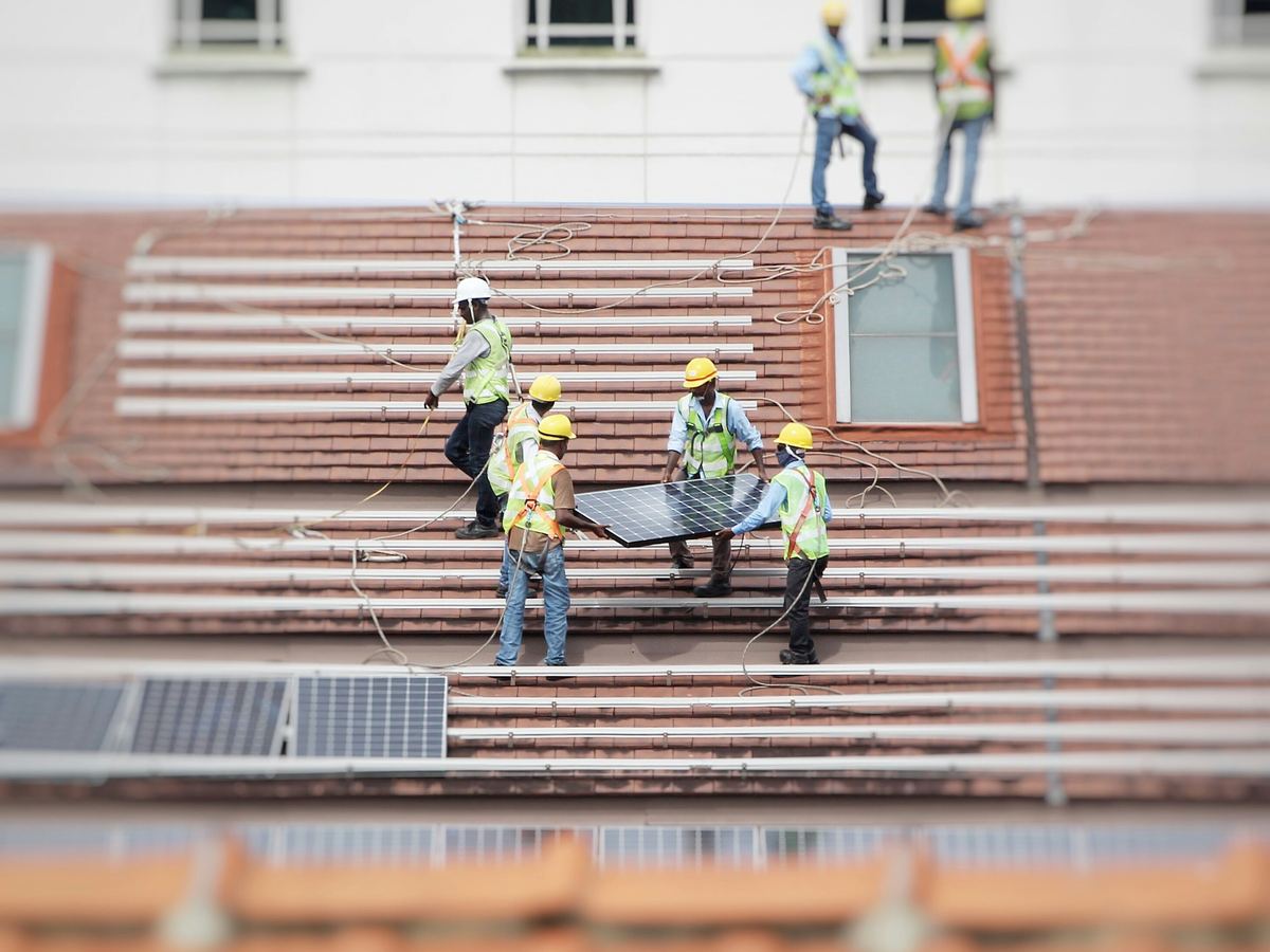 Crew in hard hats carrying a solar module across a roof