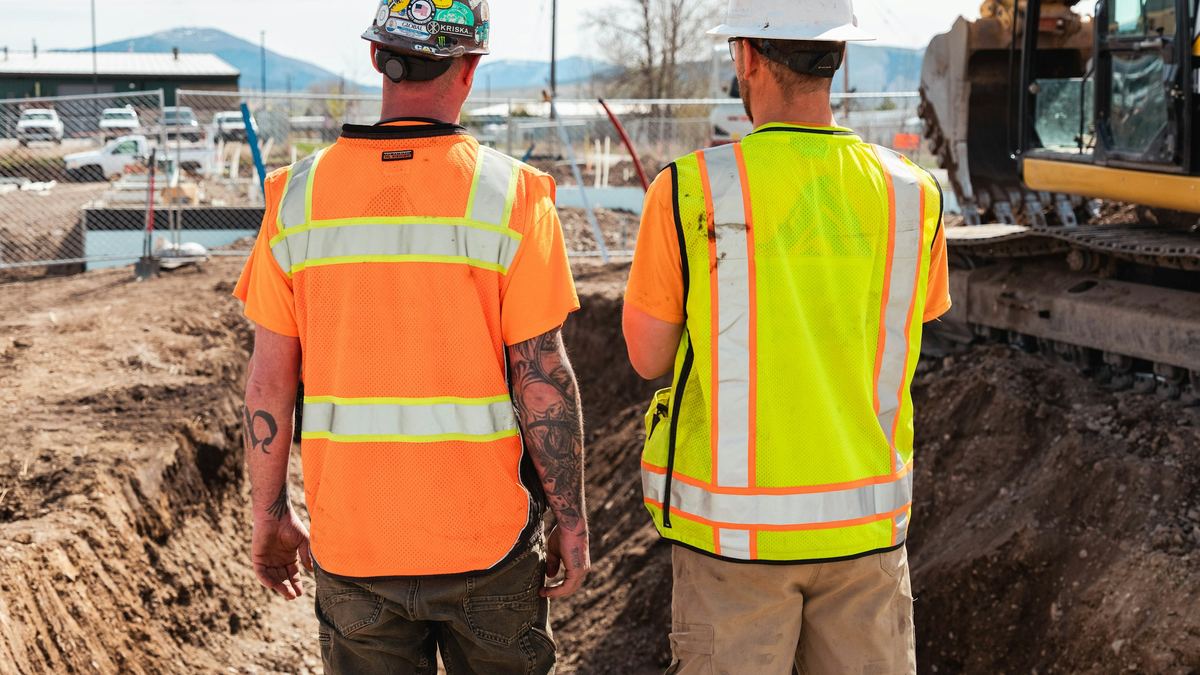 Two tradespeople in hard hats and safety vests on a construction site