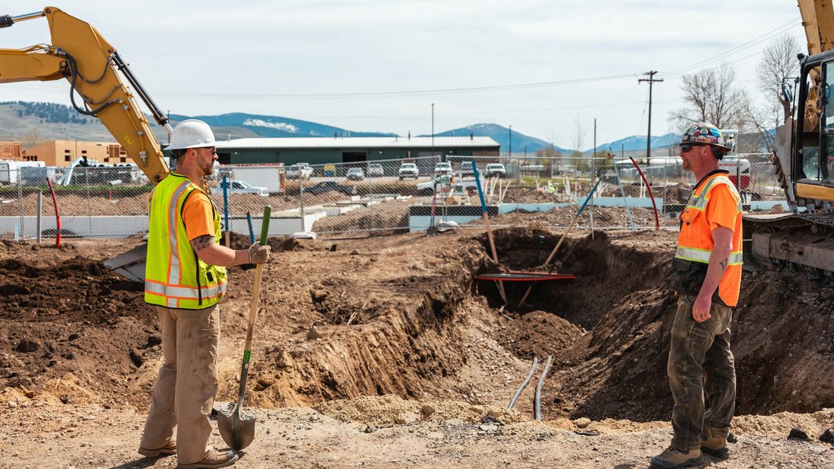 Two workers in high-visibility vests and hard hats reviewing an excavation on an active site
